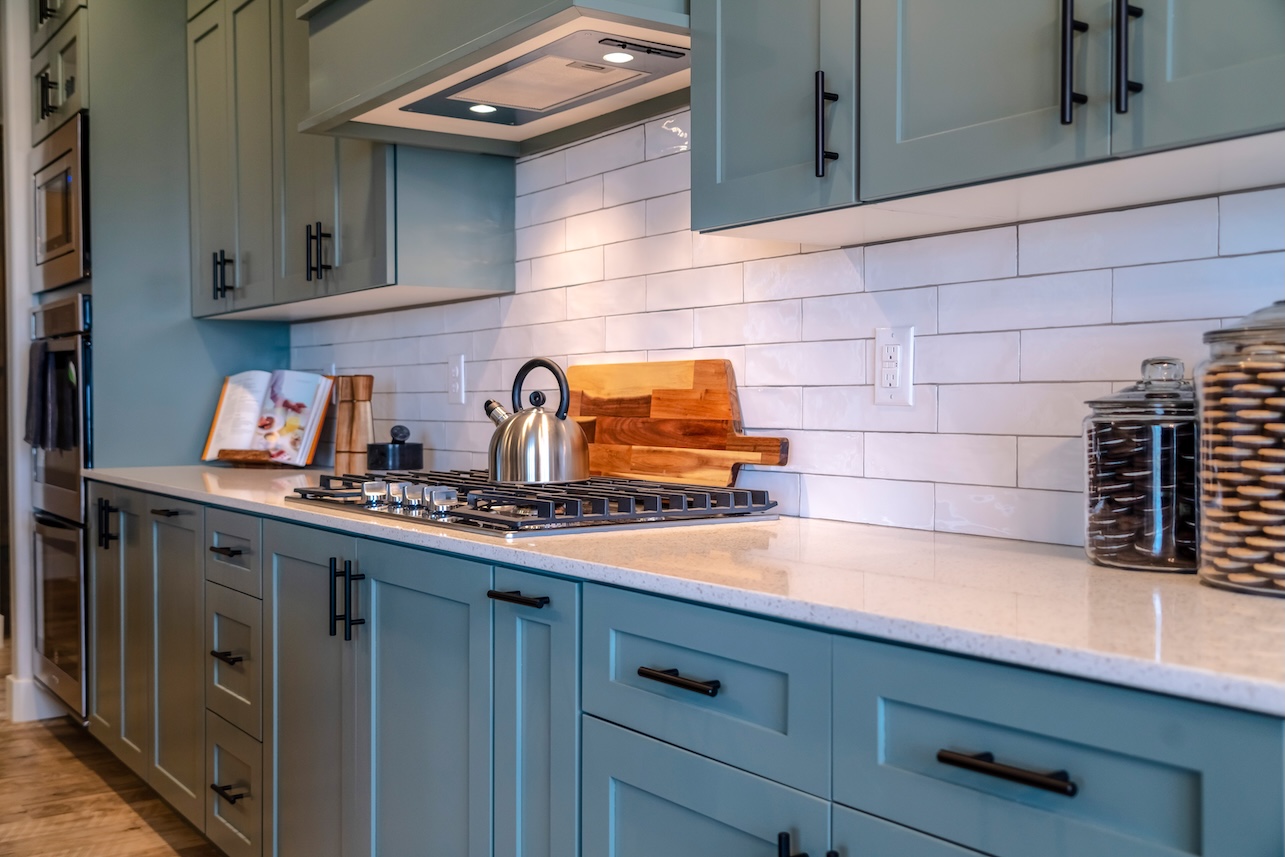 Cooking area of home with cabinets and exhaust hood over cooktop and countertop. Kitchen tools and appliances can also be seen inside the room.